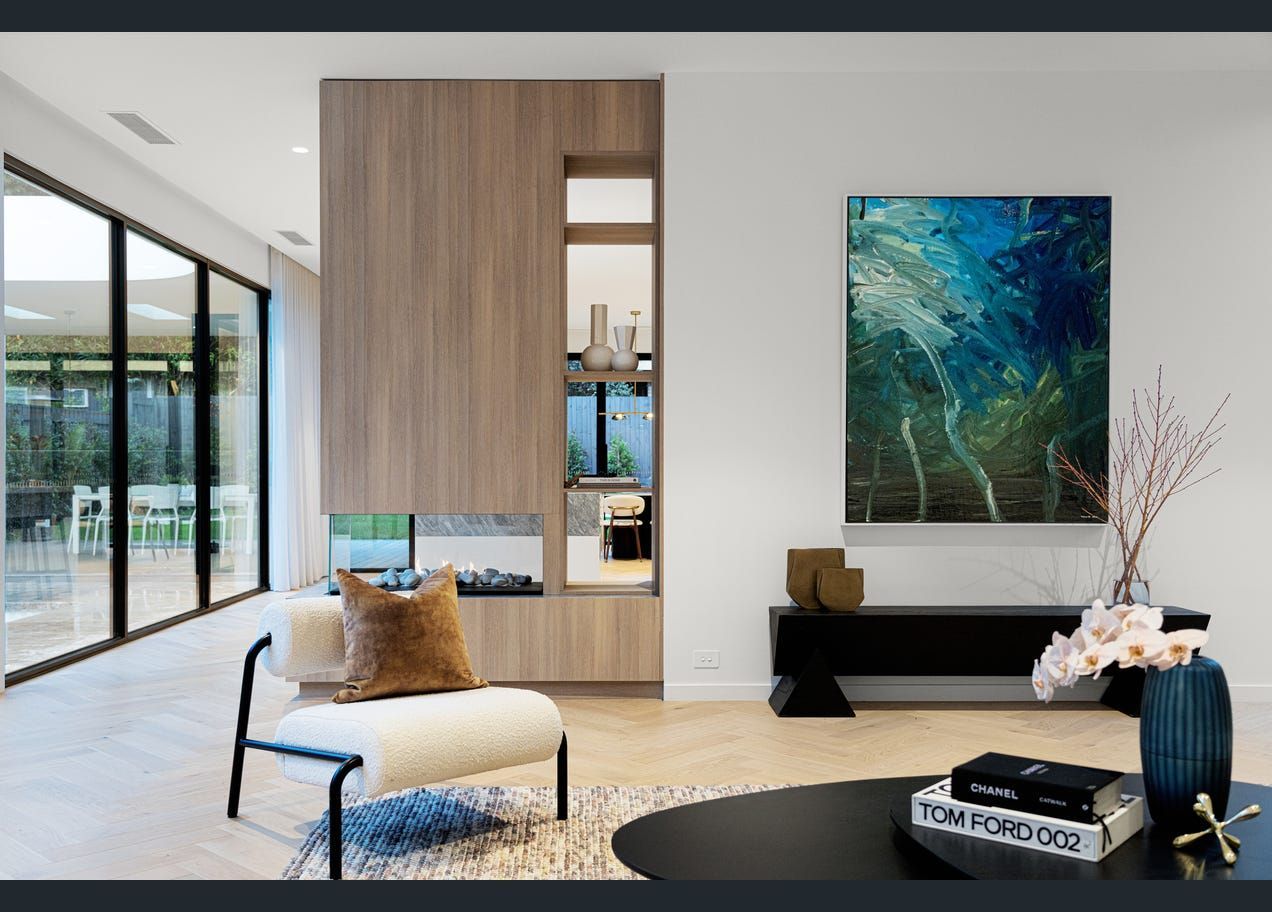 Modern living room with large windows, wood accent wall, black bench, abstract art, and light chair