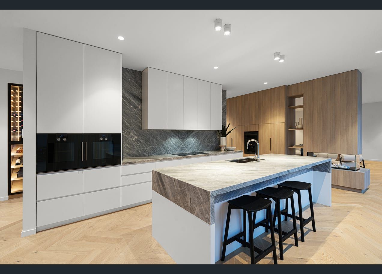 Modern open-plan kitchen with white cabinets, wood accents, marble island, and black stools