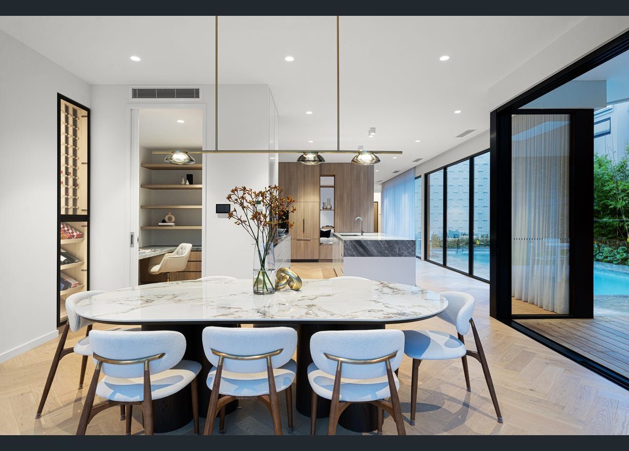 Modern open-plan dining room with marble table, white chairs, kitchen island, and floor-to-ceiling windows