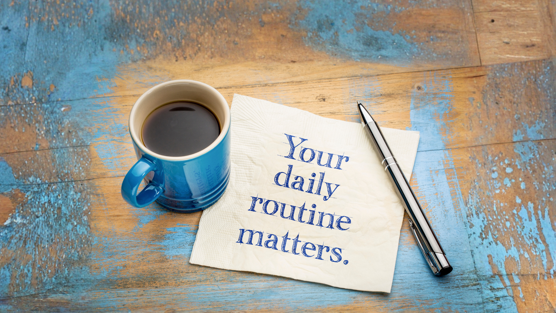 Coffee mug beside a notepad reading “Your daily routine matters” on a blue wooden desk.