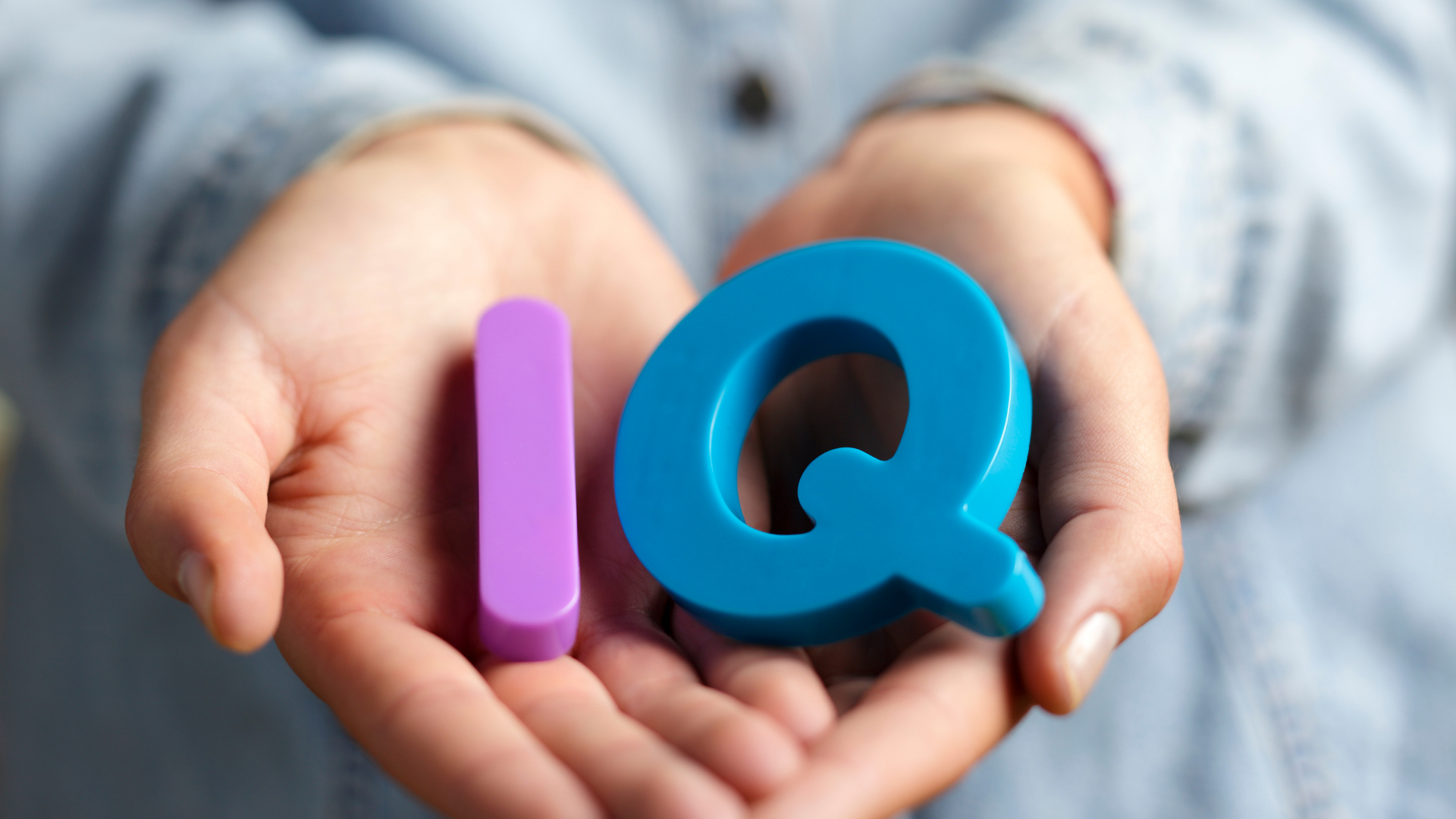 Hands holding colorful 3D letters “i” and “Q” against a blurred background