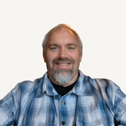 A bald man with a tattoo on his arm is standing with his arms crossed.