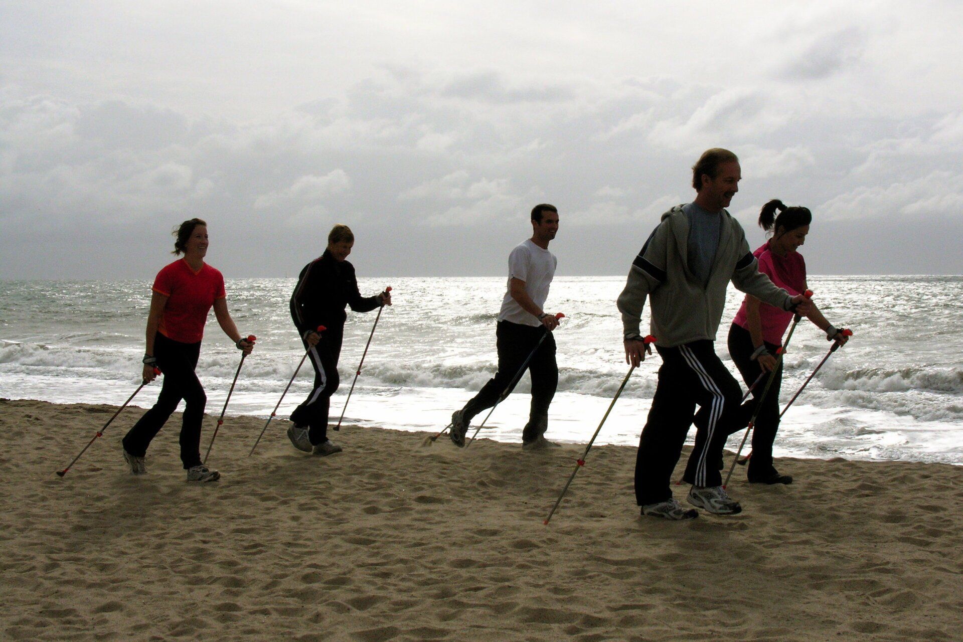A group of people are walking on the beach with walking poles
