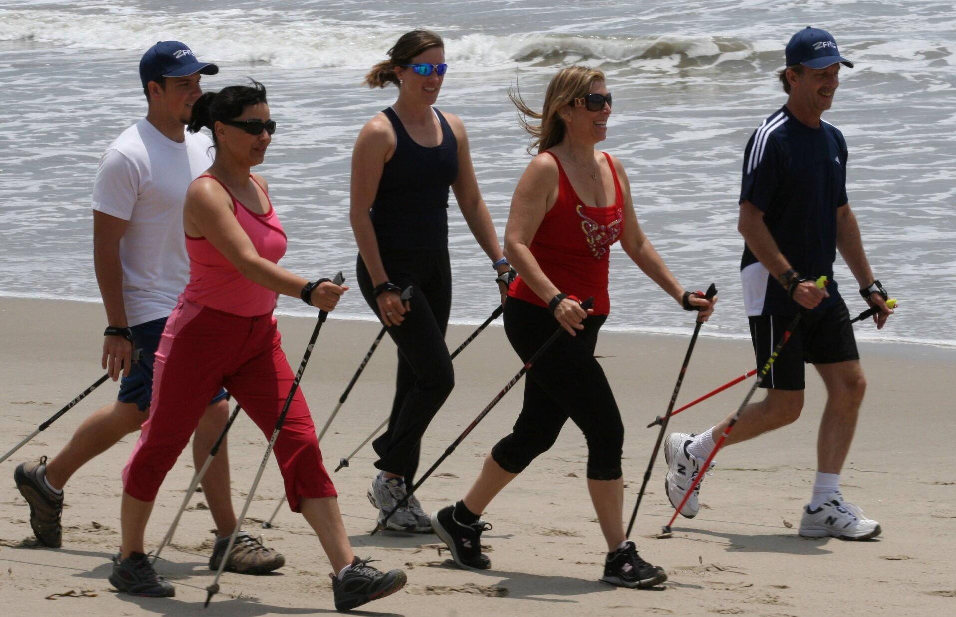 A group of people are walking on the beach with walking poles