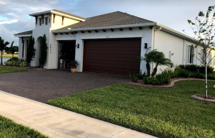 A white house with a brown garage door and a brick driveway