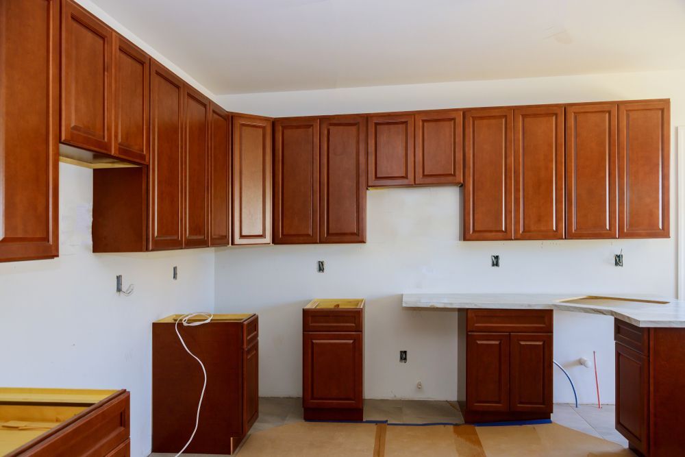 Unfinished kitchen with wooden cabinets, white walls, and exposed appliances under installation.