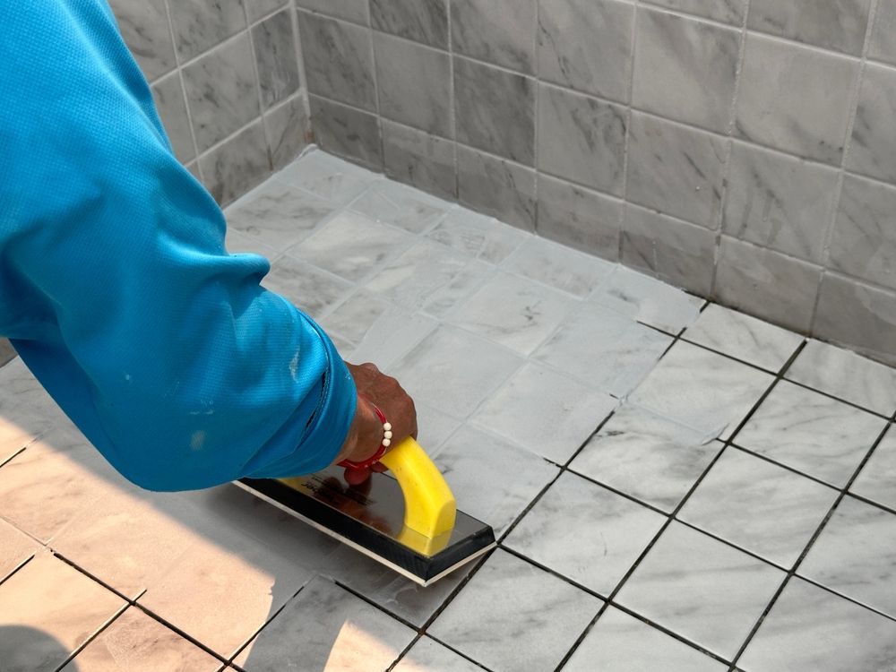 Person smoothing gray tile grout with a hand tool in a tiled room