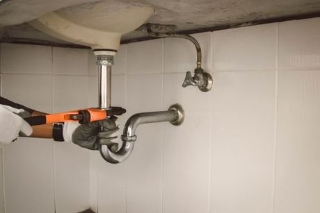 Hands using a pipe wrench to tighten a sink drain pipe under a bathroom sink
