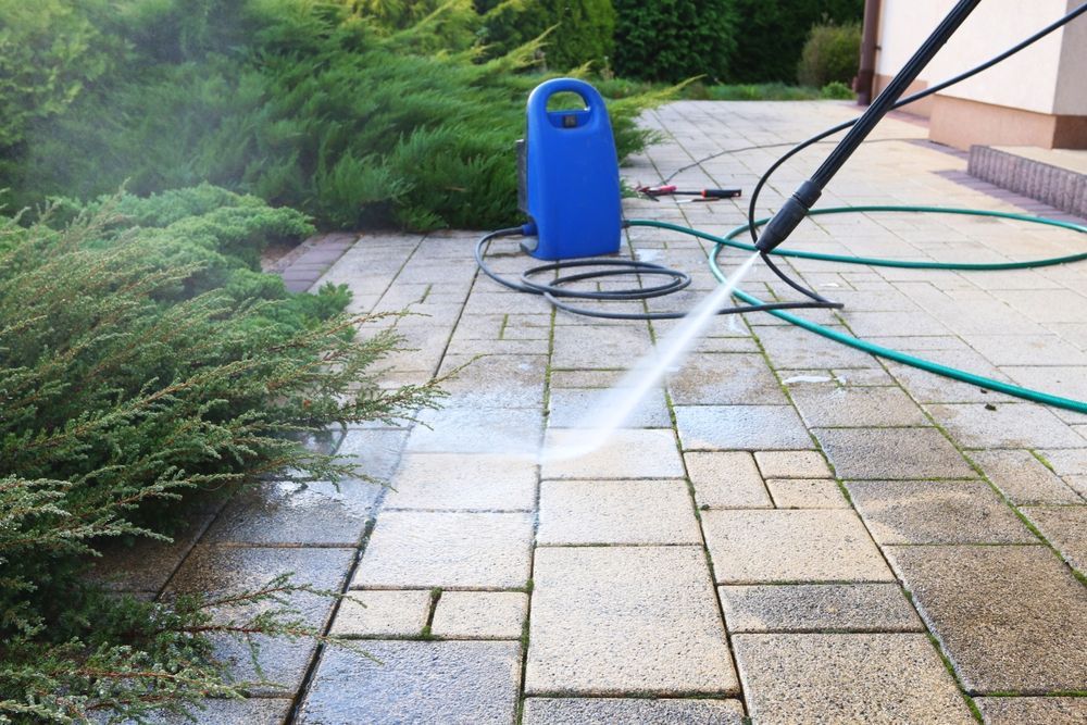 Person pressure-washing a stone patio with a blue hose reel nearby.