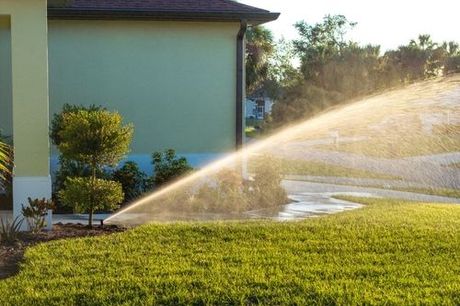 Lawn sprinkler watering green grass beside a house in bright sunlight