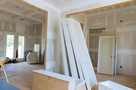 Unfinished interior room with stacked drywall sheets and wood trim during renovation