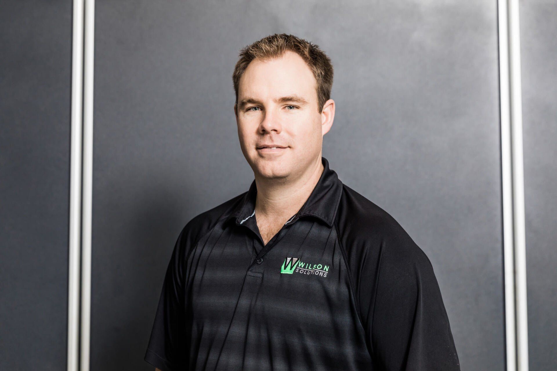 A man in a black shirt is standing in front of a blackboard.