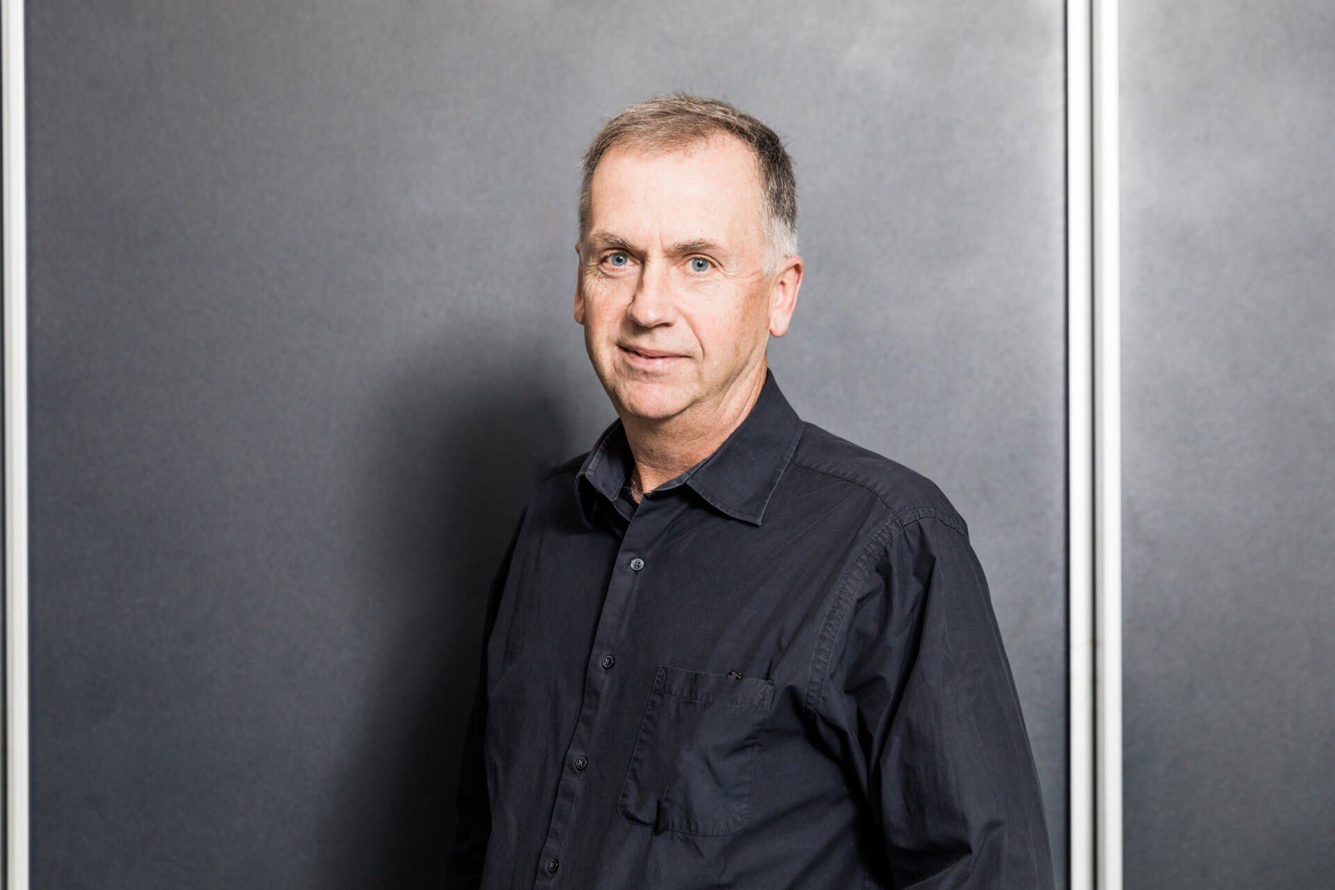 A man in a black shirt is standing in front of a blackboard.