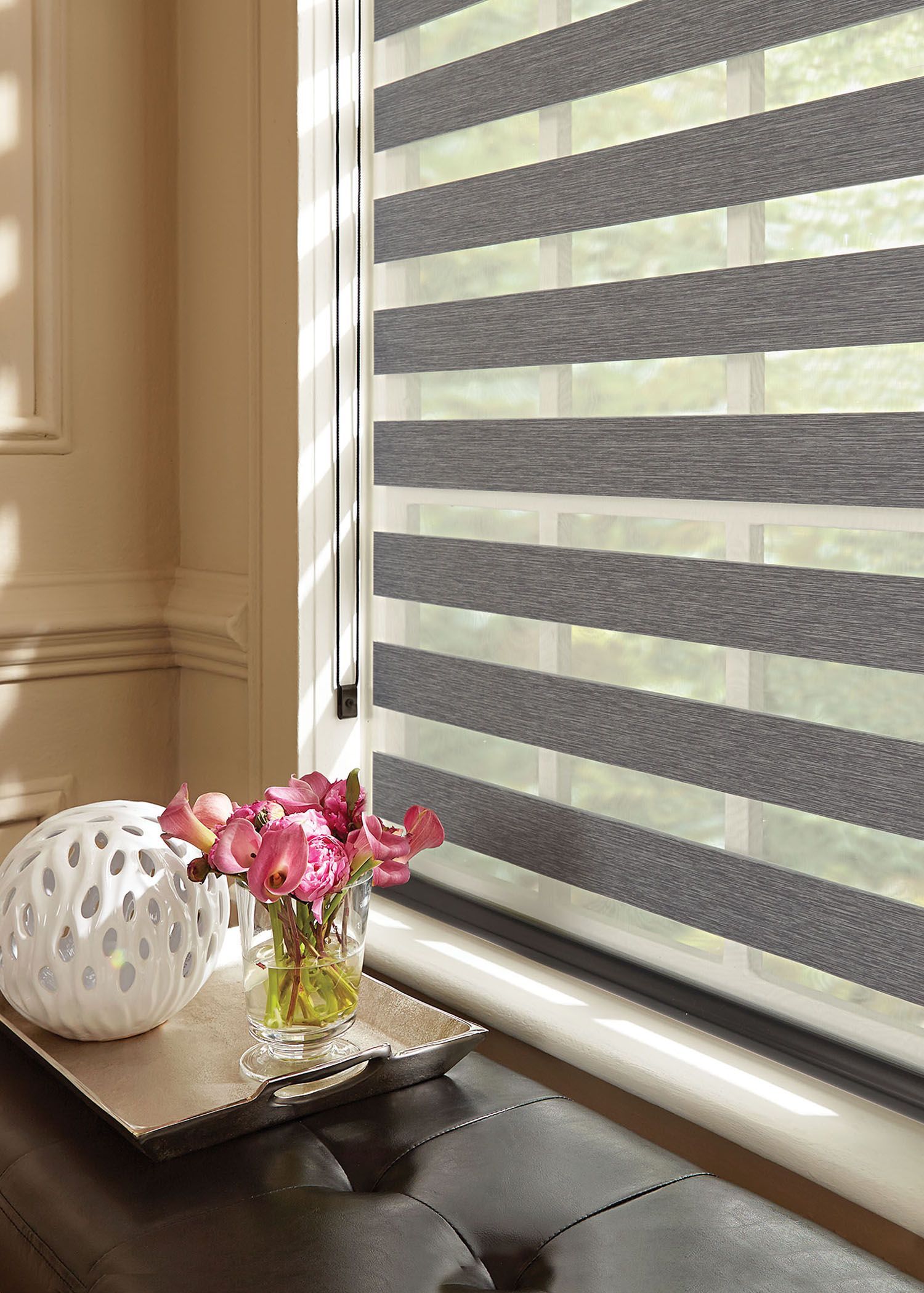 A window with a striped blind and a vase of flowers on a table.