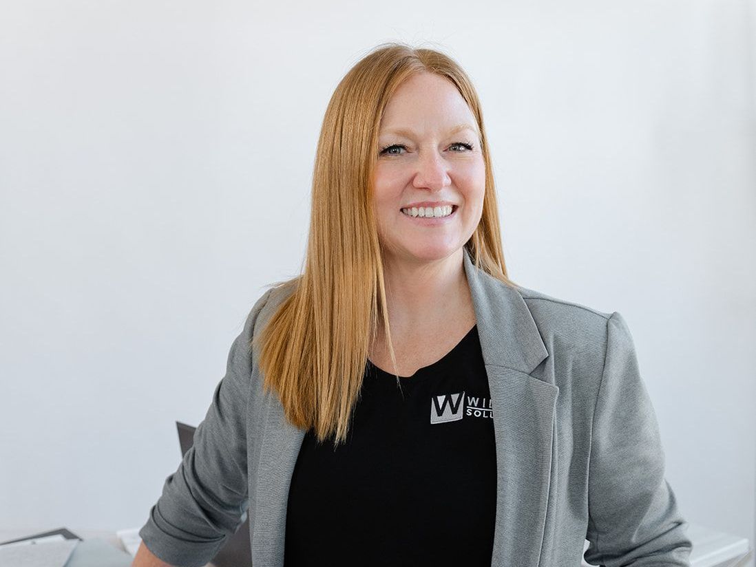 A woman wearing a gray jacket and a black shirt is smiling for the camera.