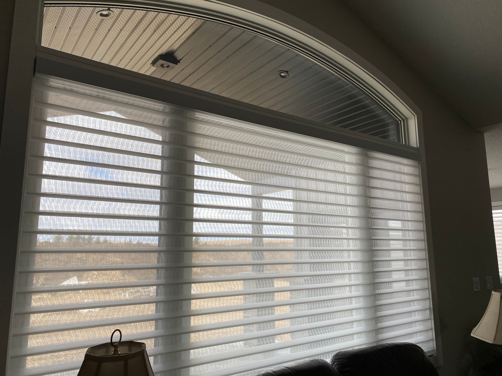 A living room with a large window and white blinds on it.