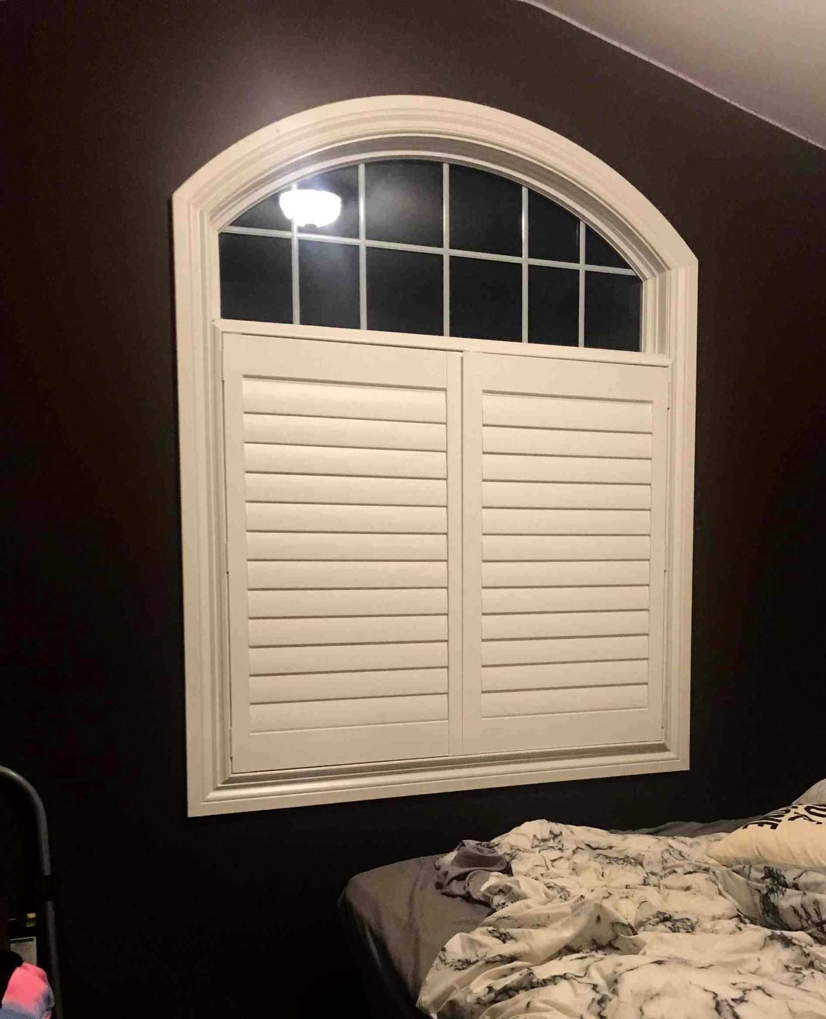 A bedroom with a large arched window and white shutters.