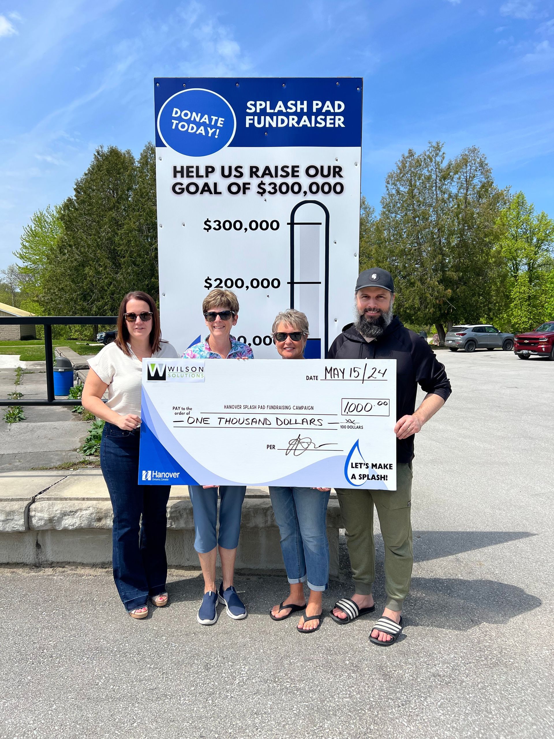 A group of people holding a large check in front of a sign.