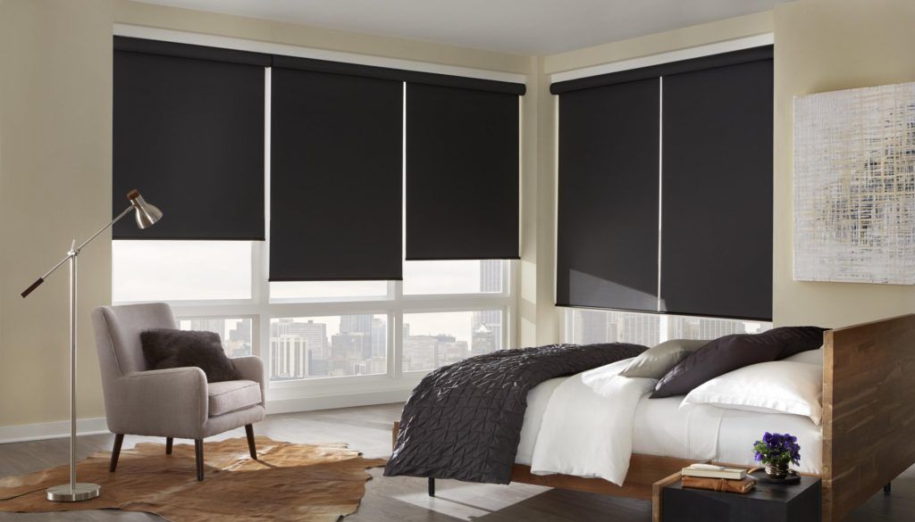 A bedroom with a bed , chair , lamp and black blinds.