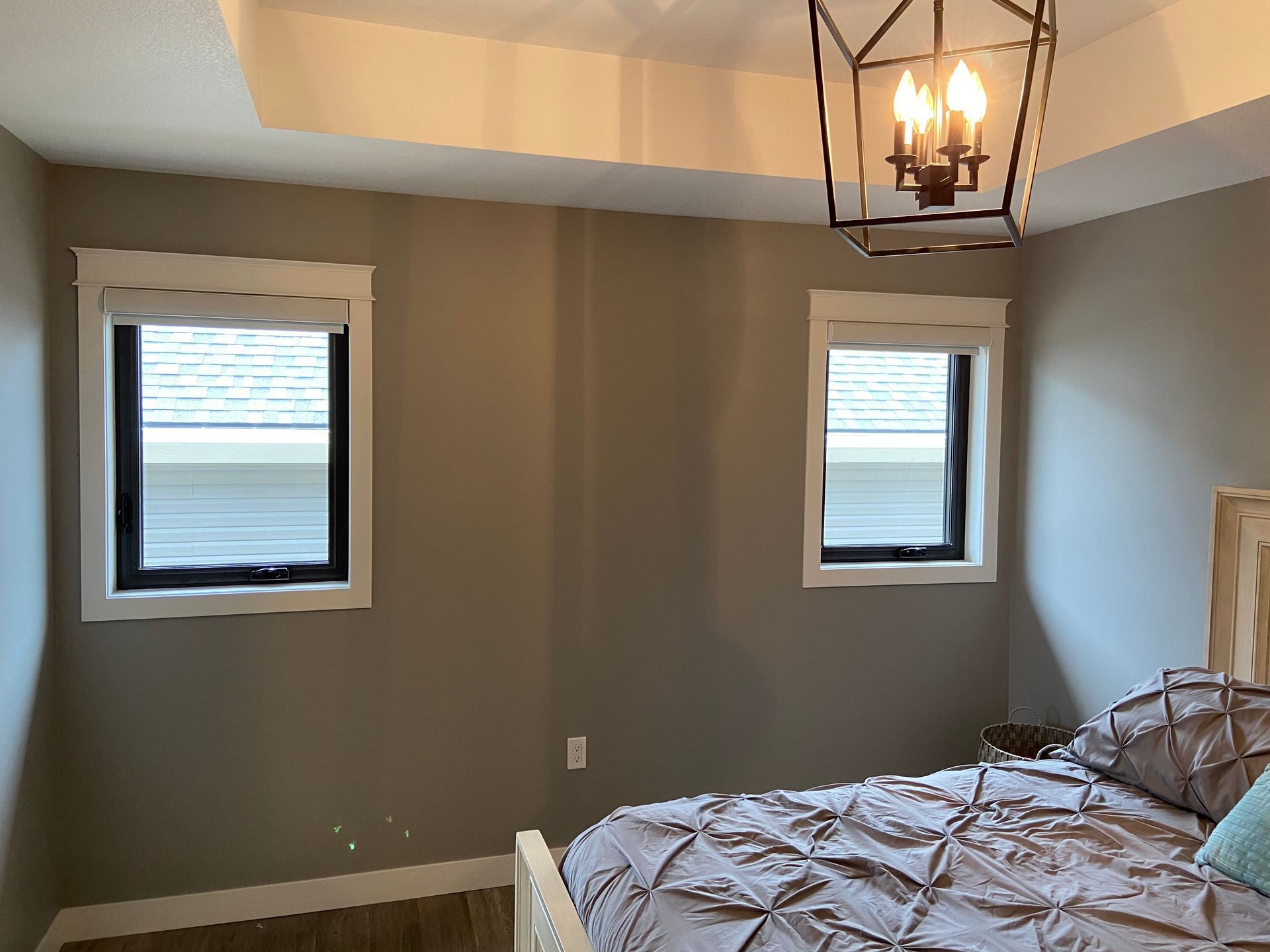 A bedroom with a bed , two windows and a chandelier.