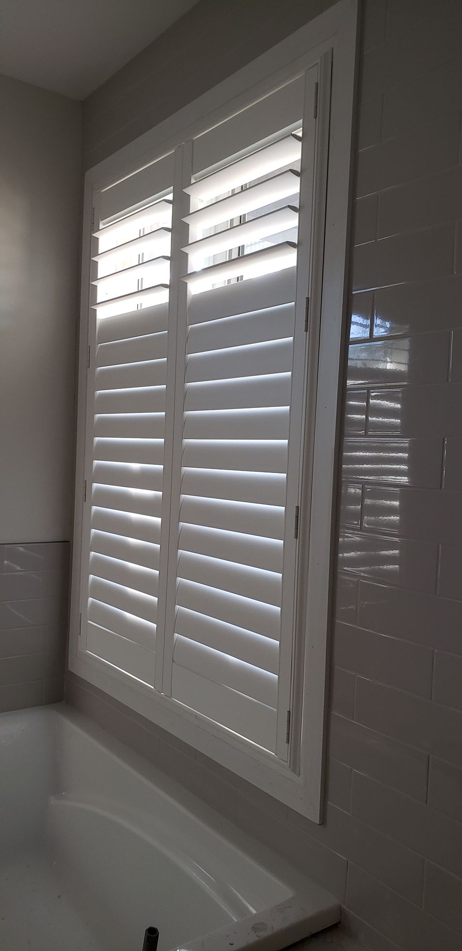 A bathroom window with white shutters and a bathtub.