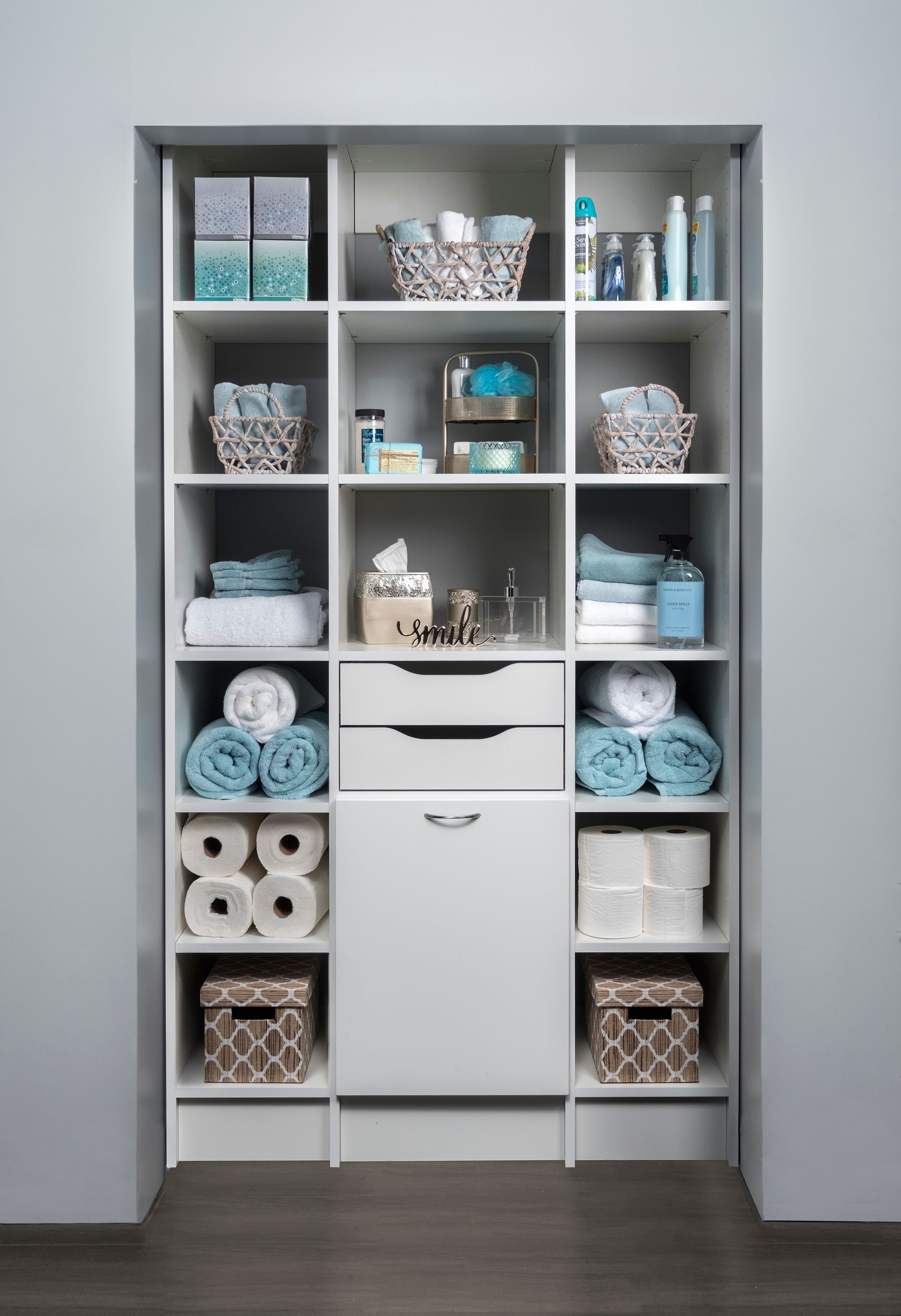 A bathroom closet filled with toilet paper , towels , baskets , and a drawer.
