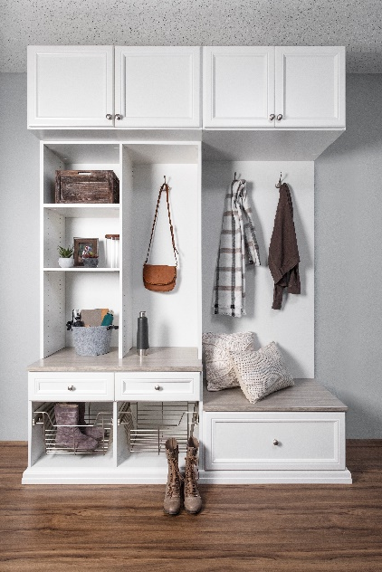 White entryway cabinet with storage, bench, and hooks. Tan handbag and jackets hang. Boots on the floor.
