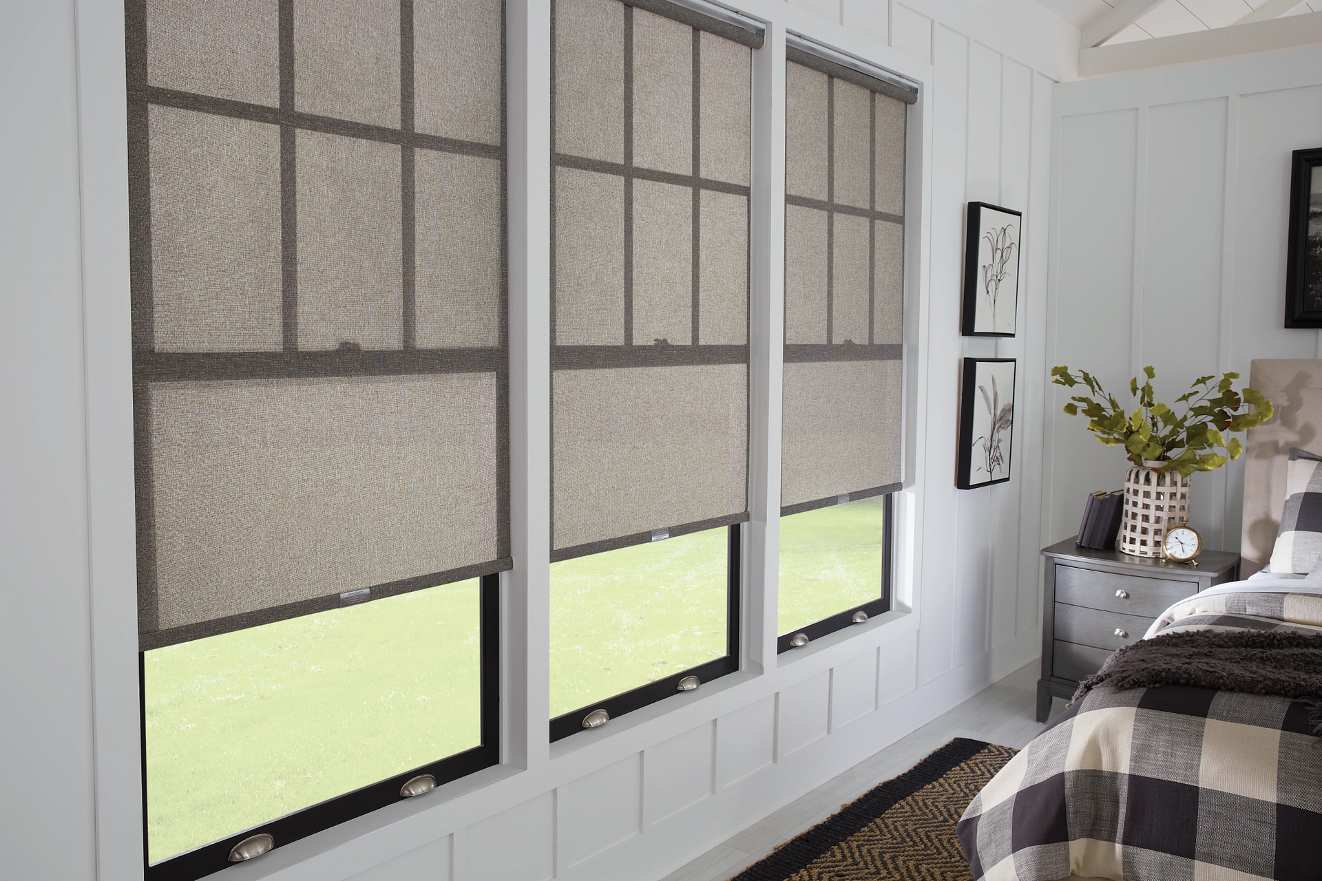 A bedroom with three windows and a bed with a plaid comforter.