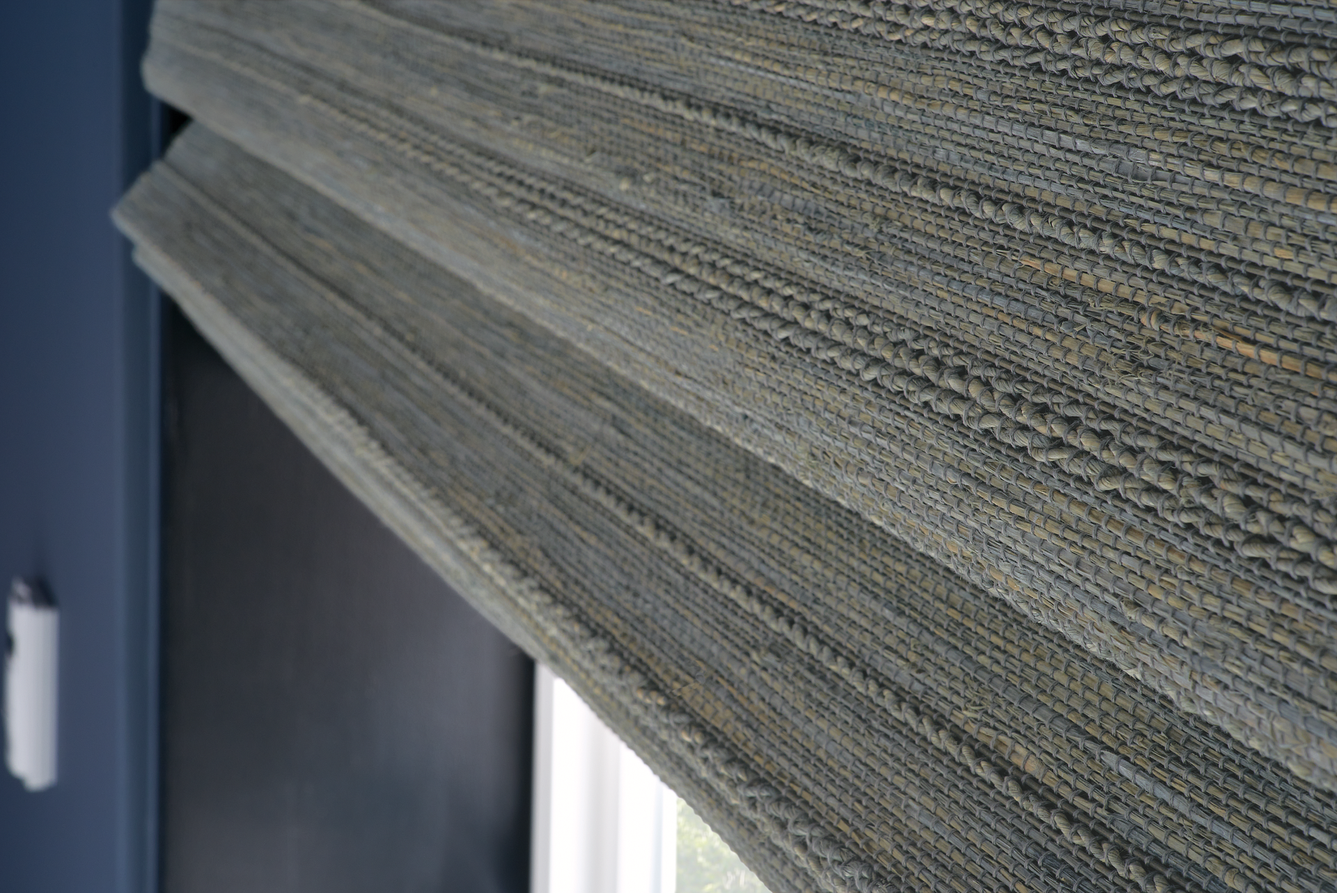 A close up of a gray roman shade on a window.