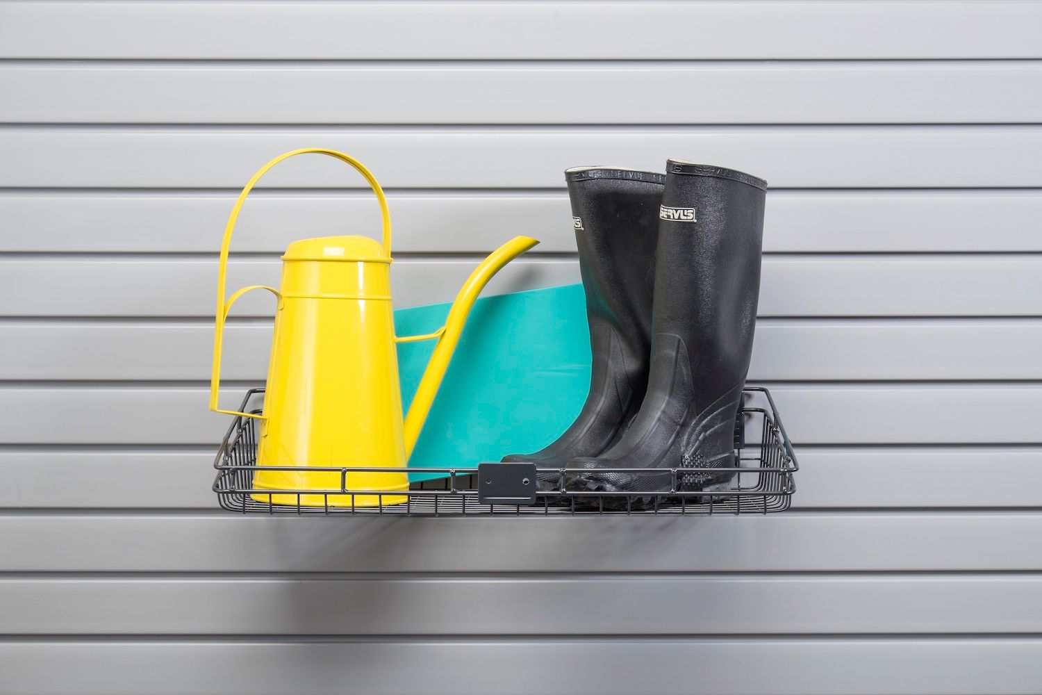 Yellow watering can, teal mat, black boots on a wire shelf attached to a slatted gray wall.