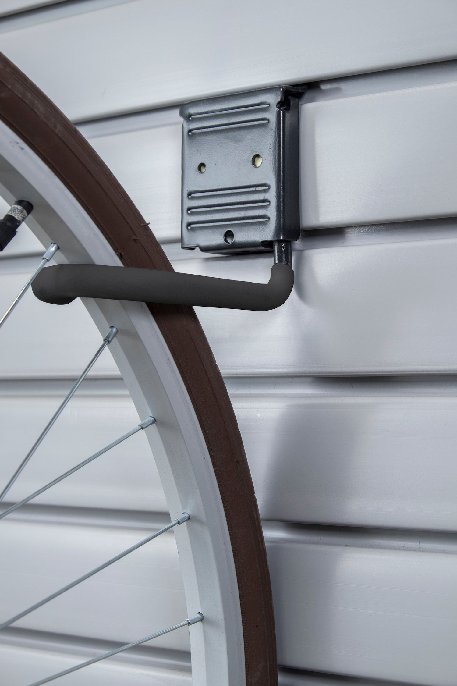 Bicycle wheel hanging on a black hook attached to a white slotted wall. Brown tire.