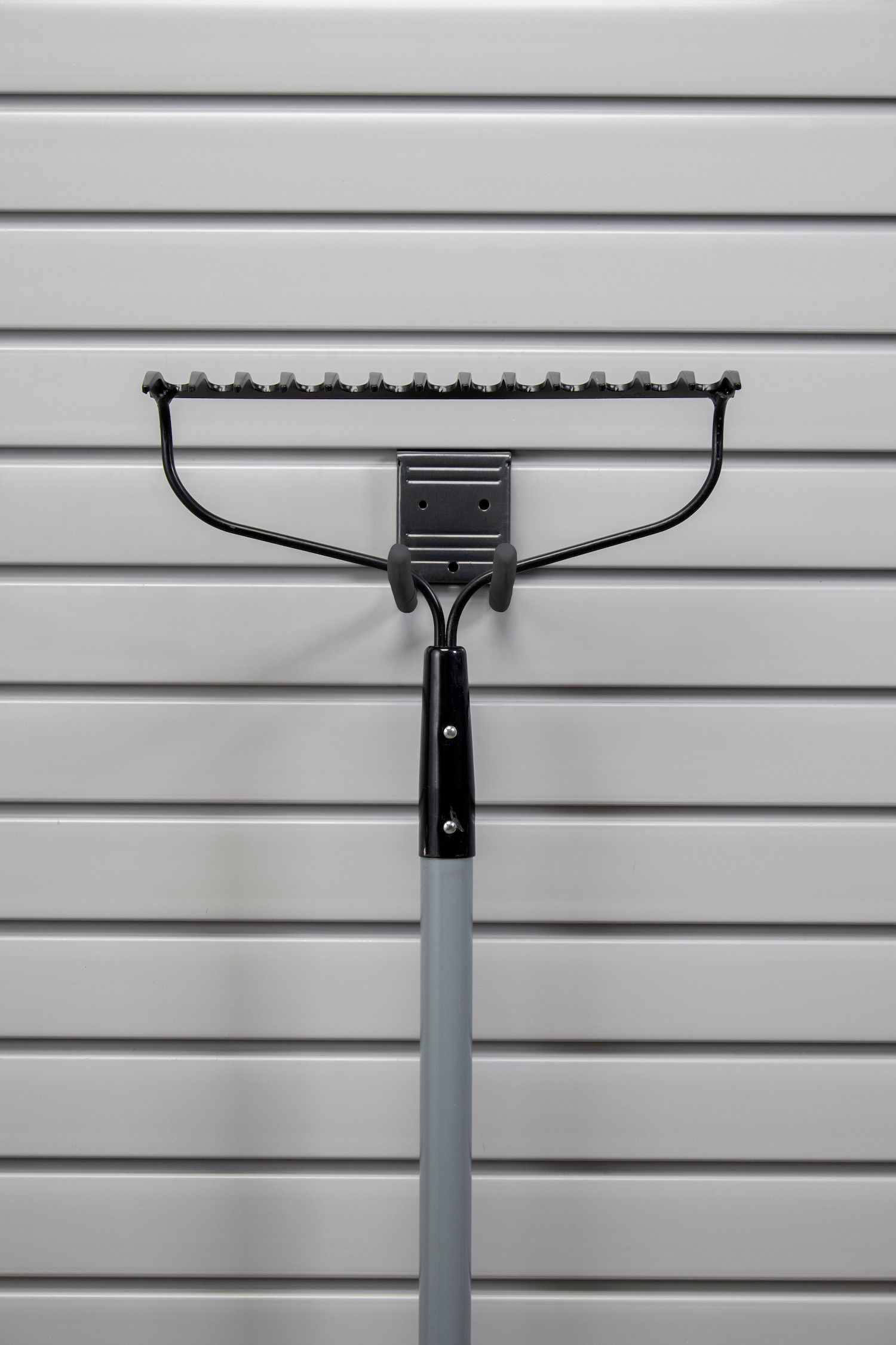 Grey rake hanging on a white slat garage wall.