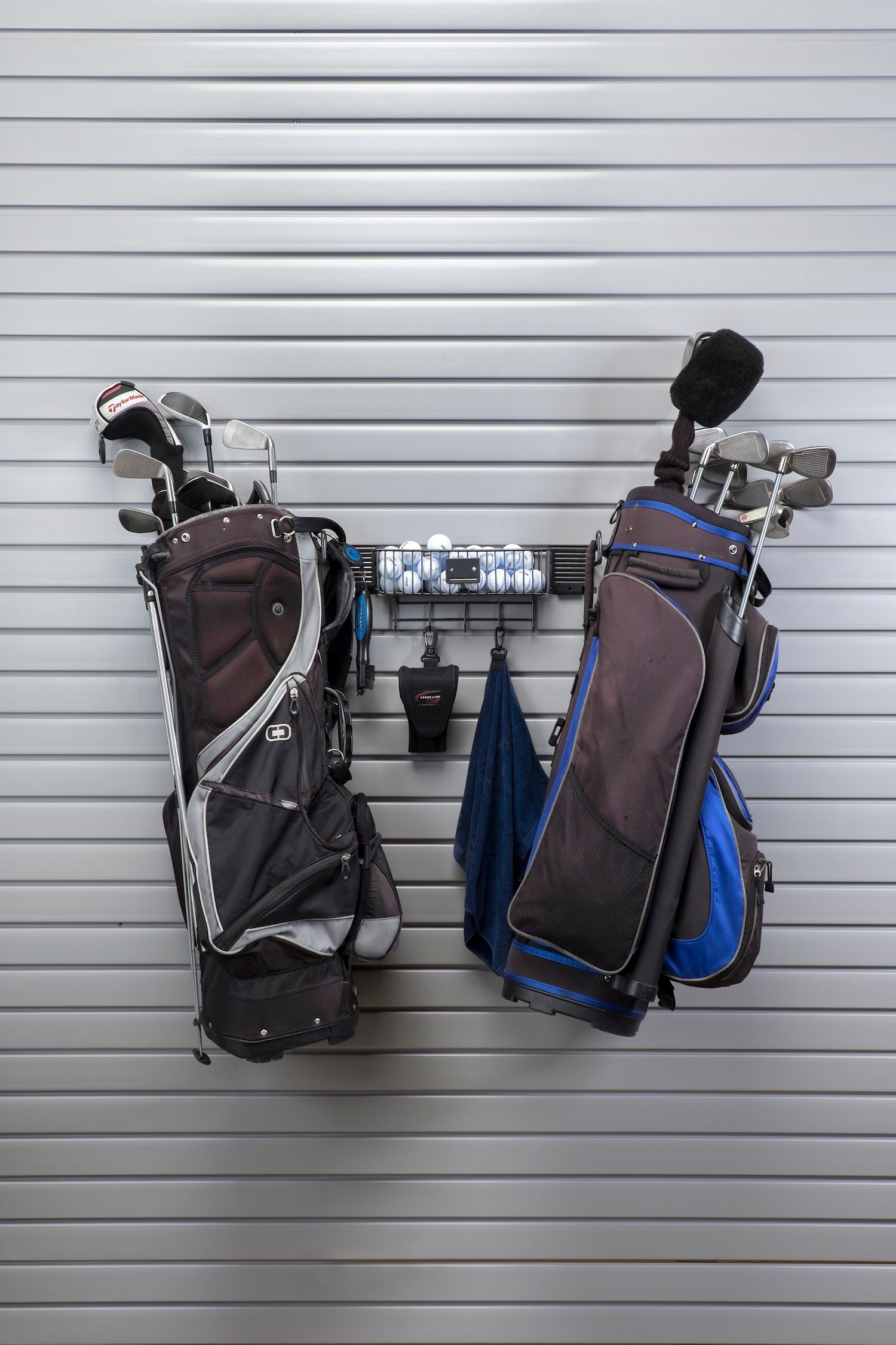 Golf bags hanging on a slat wall in a garage.