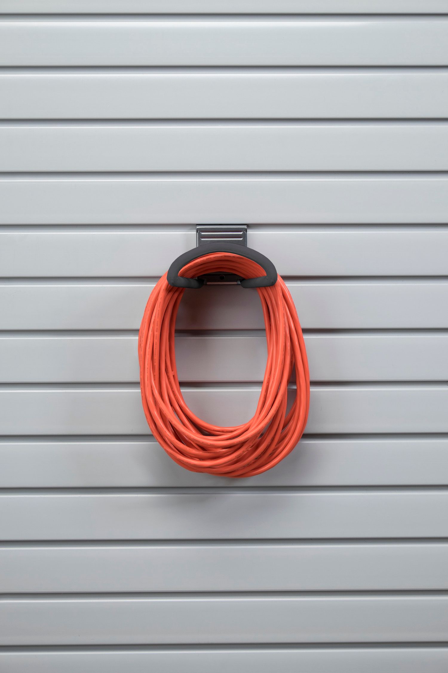 Orange extension cord coiled and held by a black hook on a gray slatted wall.
