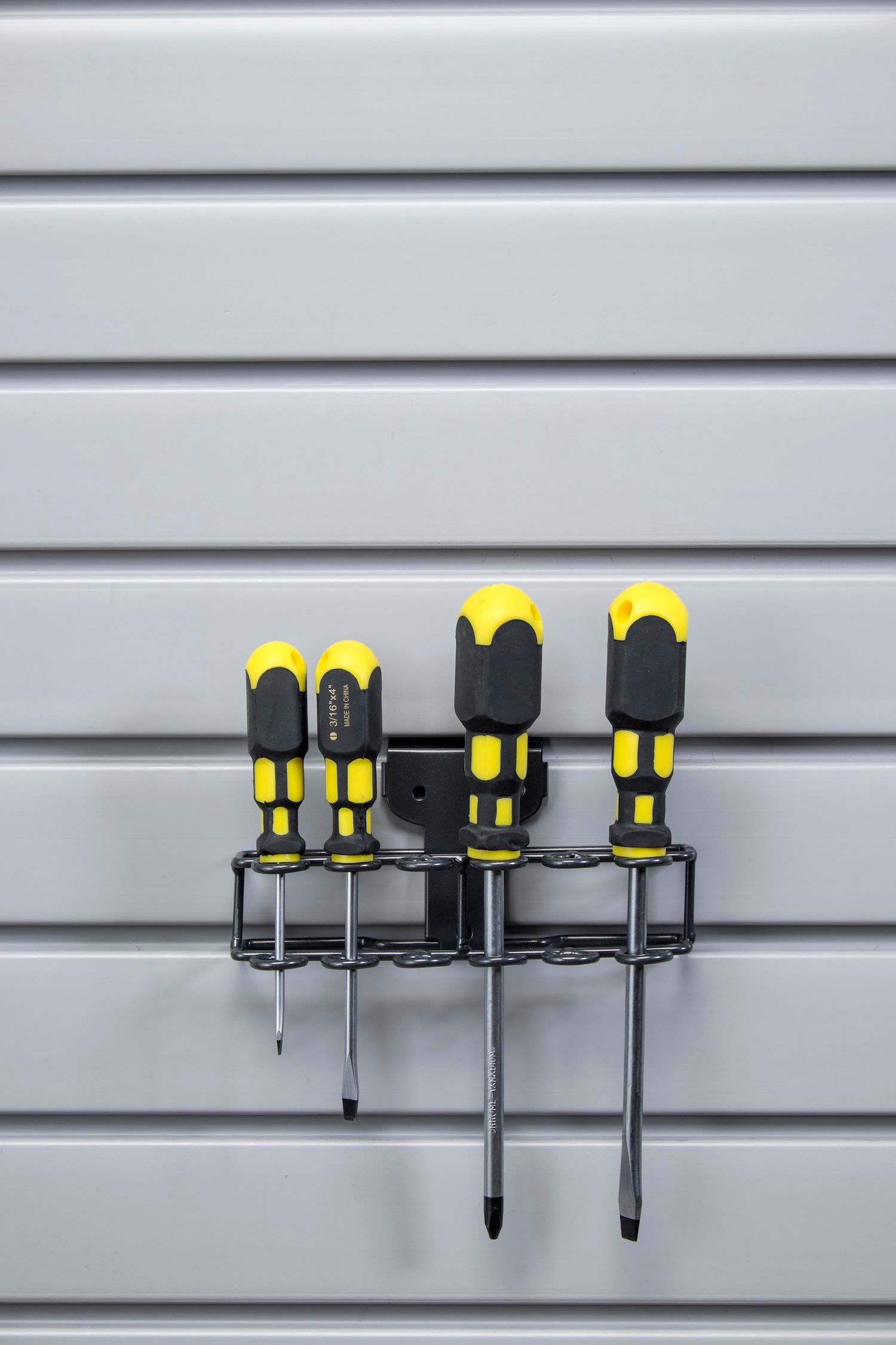 Five screwdrivers with yellow and black handles in a wall-mounted holder against a gray, horizontally-lined wall.