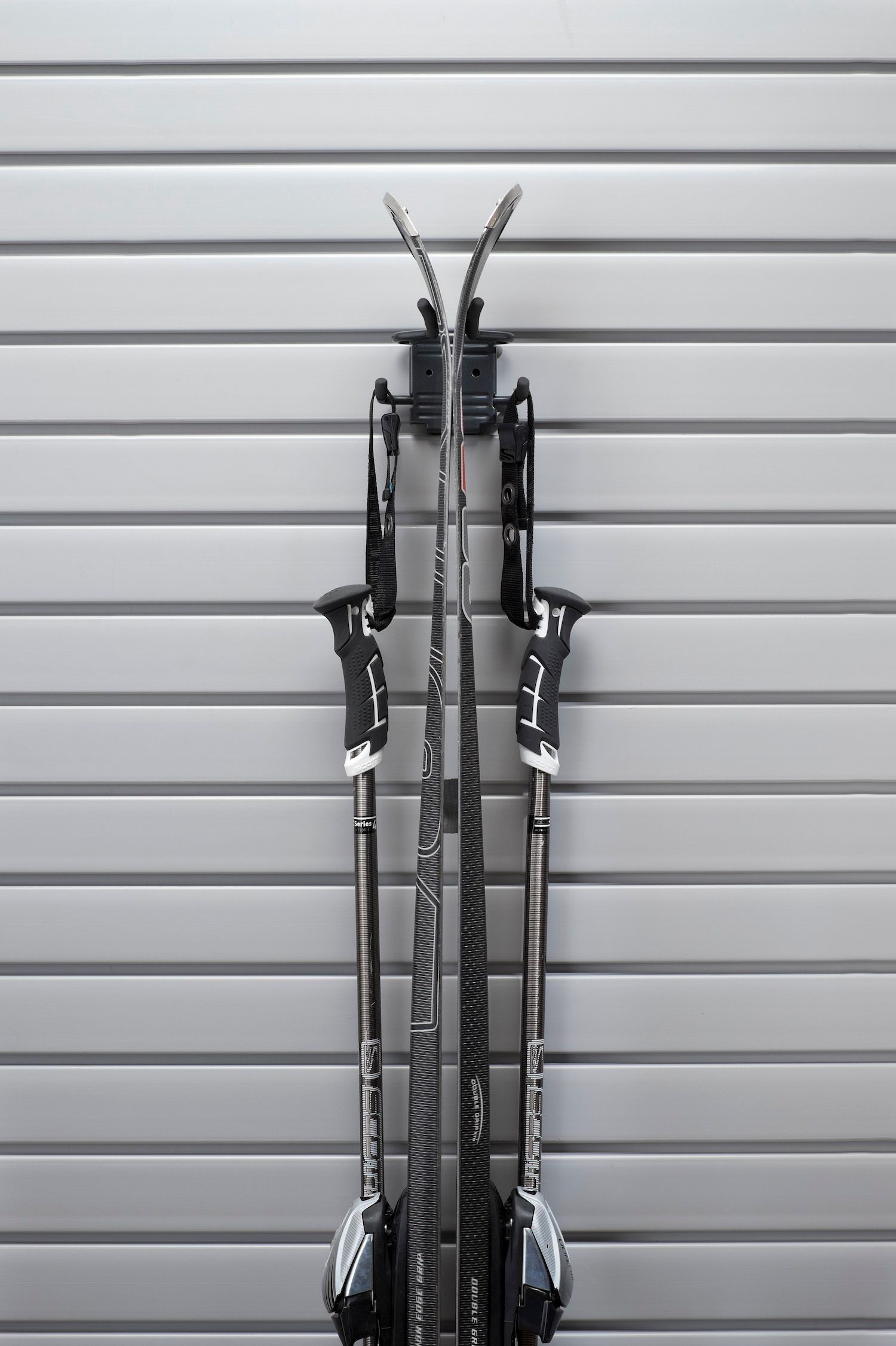 Pair of skis and poles mounted vertically on a gray, slatted wall.