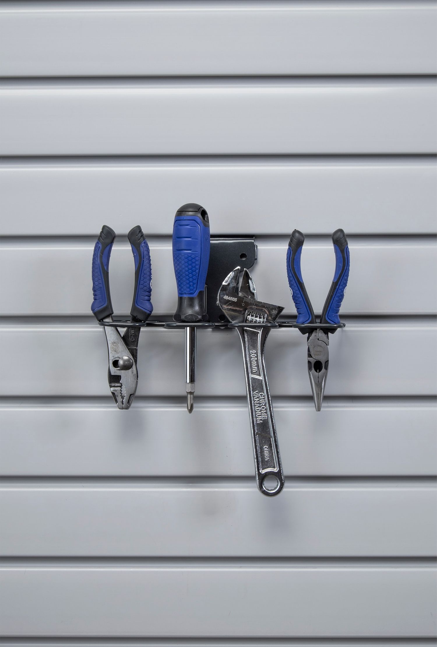Tool rack with pliers, screwdriver, and wrench hanging on a white slat wall.