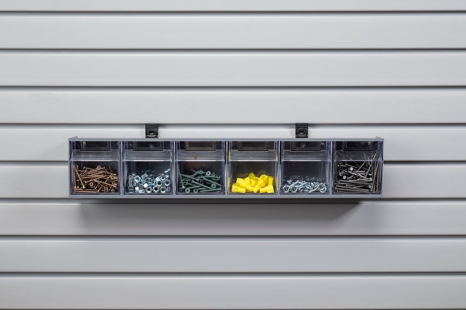Clear storage containers with screws and fasteners mounted on a slotted wall.