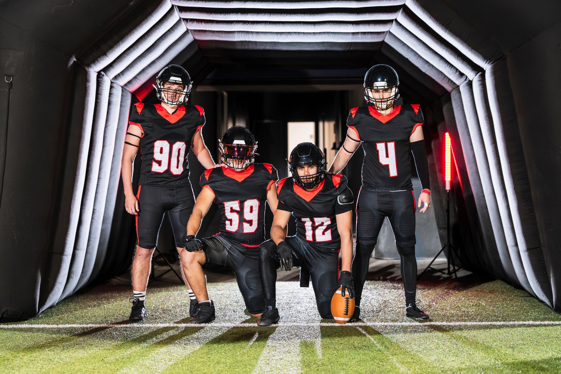 Four football players in black and red uniforms pose in a tunnel before a game