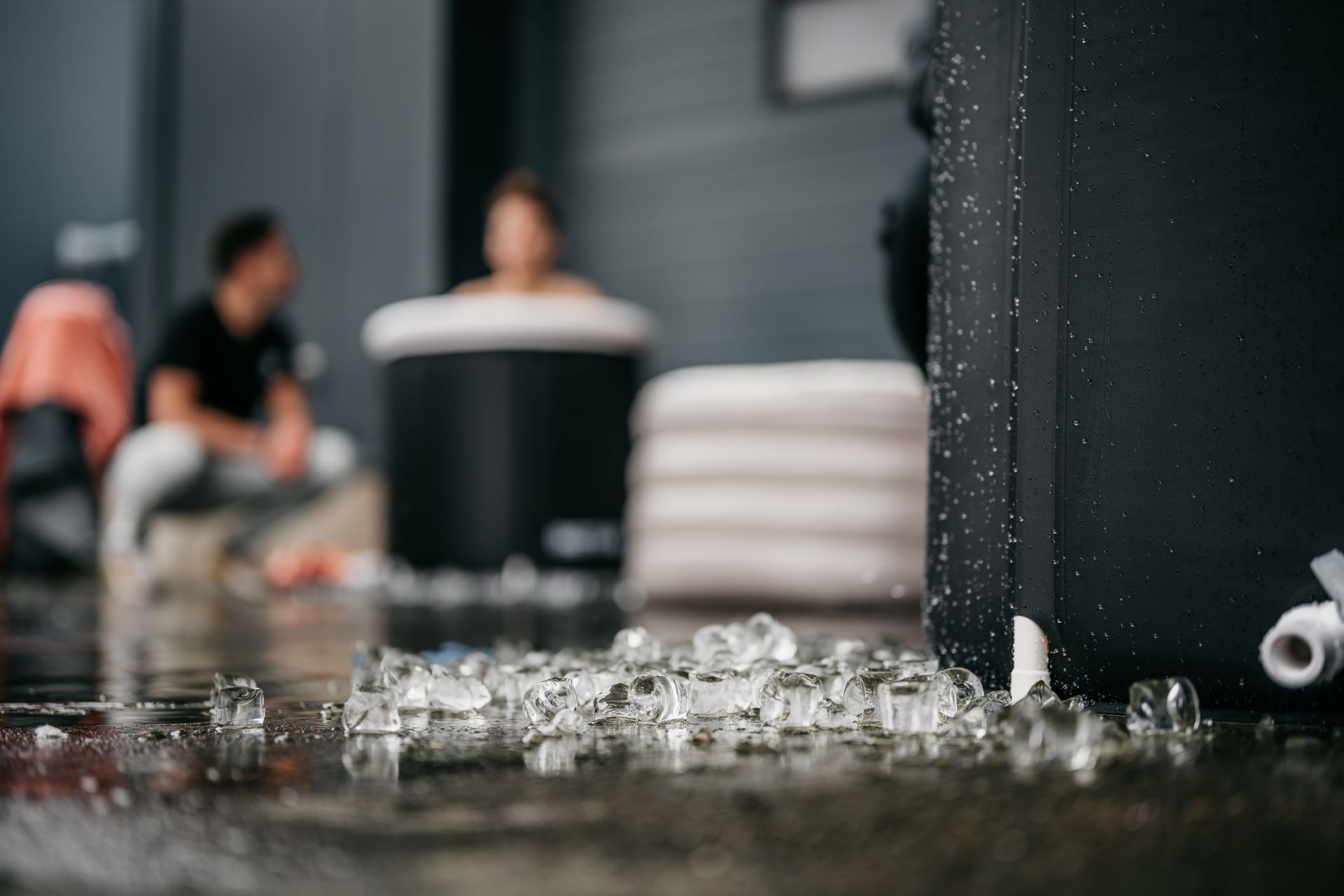 Broken glass scattered on a wet floor in a blurred indoor room, with people in the background.