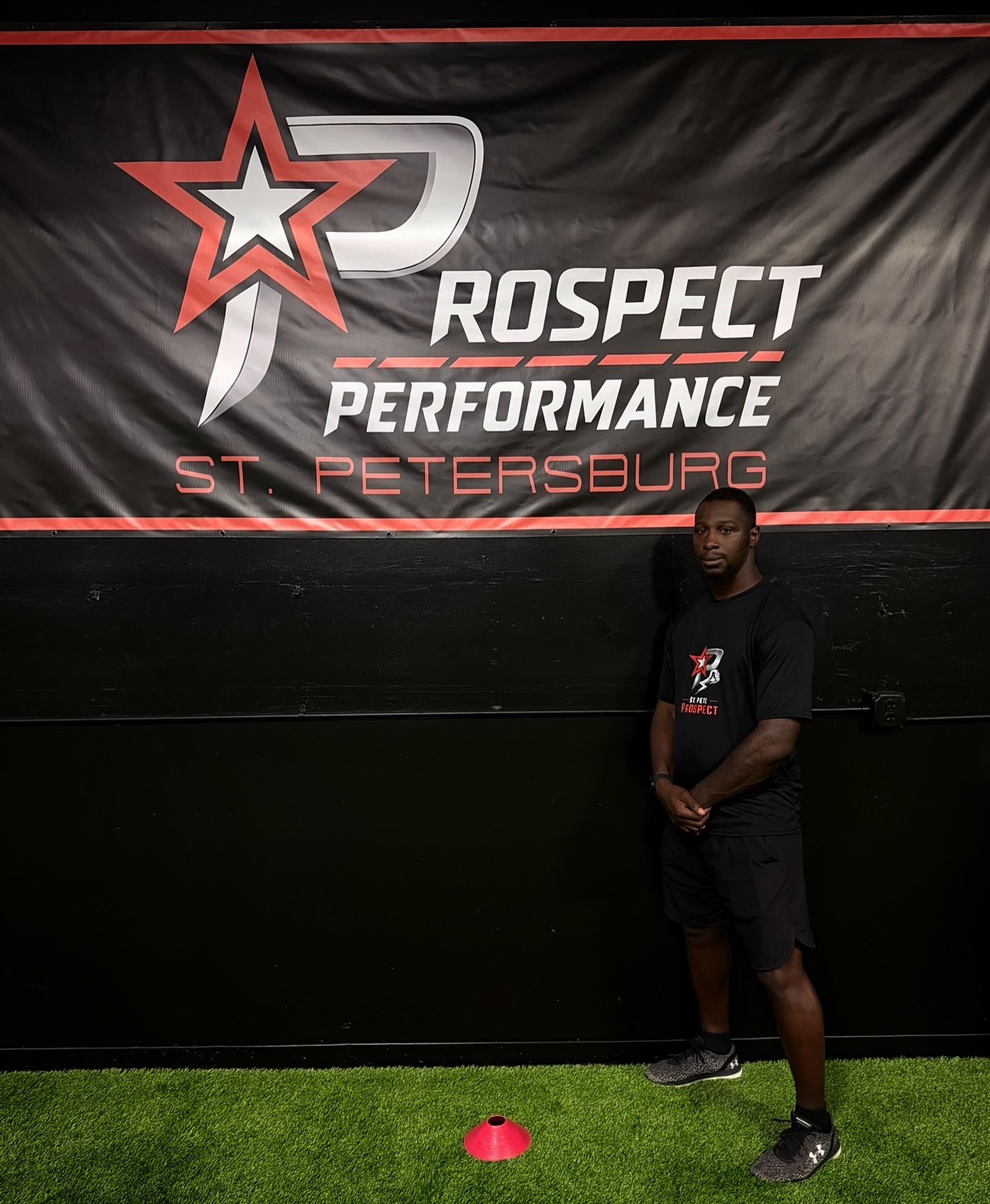 Person standing in front of a Prospect Performance St. Petersburg banner on indoor turf