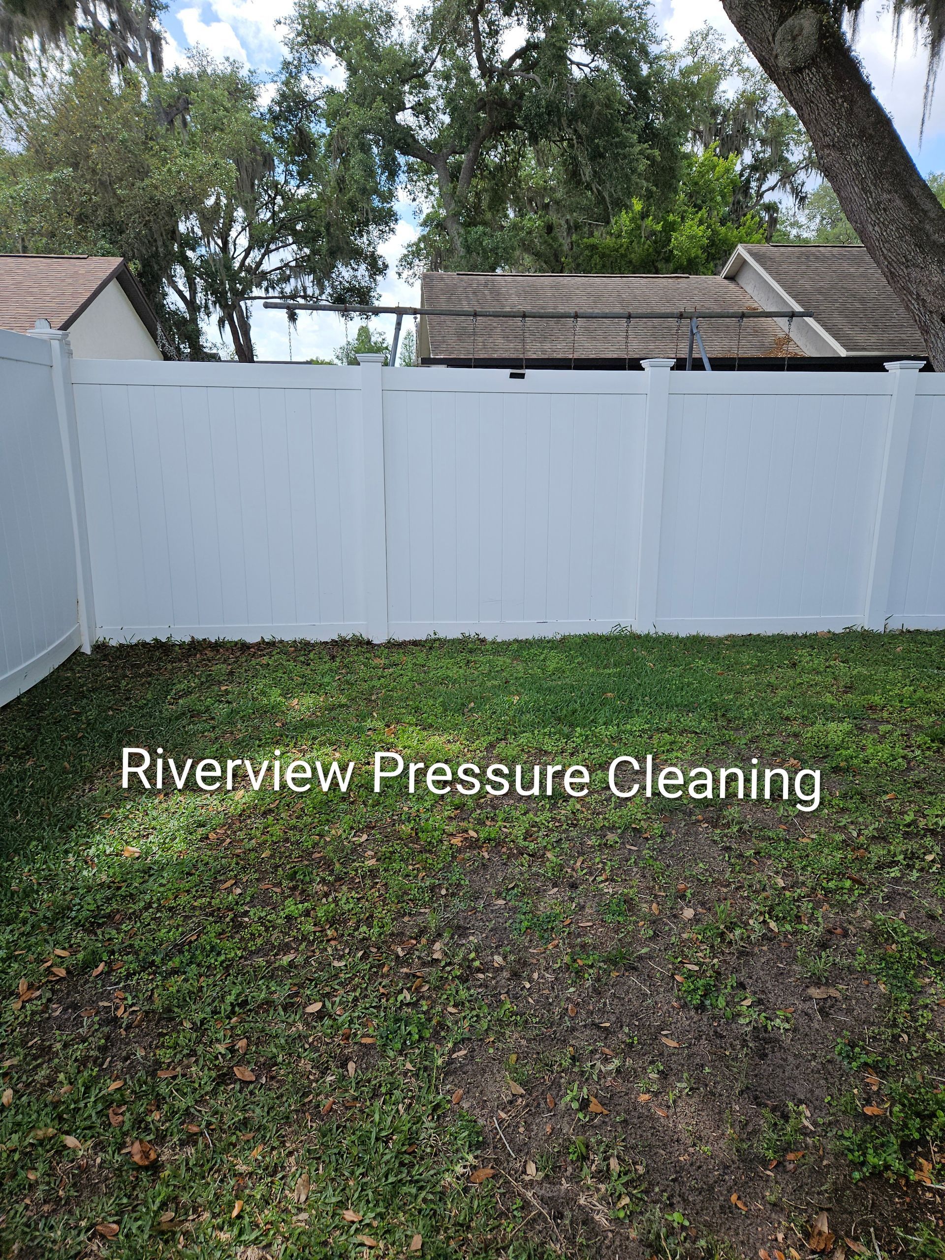 White vinyl fence and grassy backyard with trees; “Riverview Pressure Cleaning” text overlay.