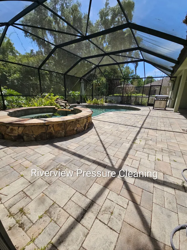 Screened outdoor patio with stone planter, pavers, and trees under a black metal roof