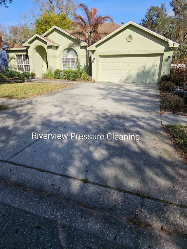 Single-story pale green house with two-car garage and long driveway in autumn sunlight