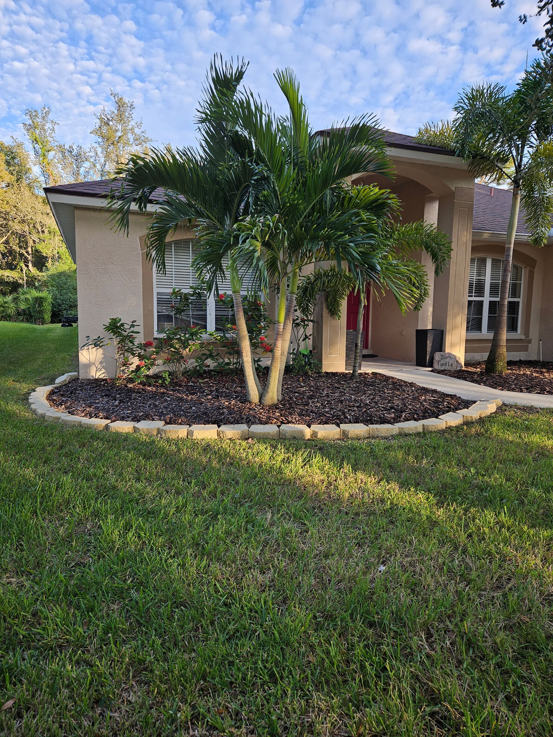 Suburban house with palm trees, landscaped front yard, and green lawn under a blue sky