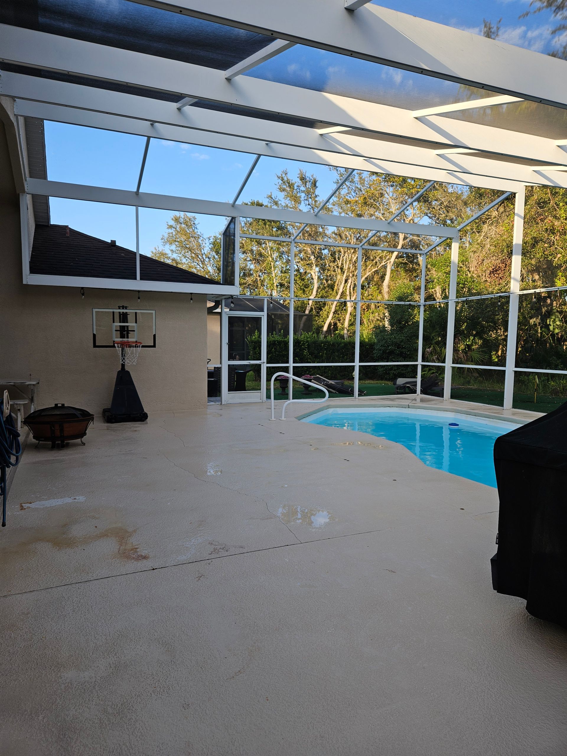 Covered patio with pool, basketball hoop, and TV overlooking a sunny backyard