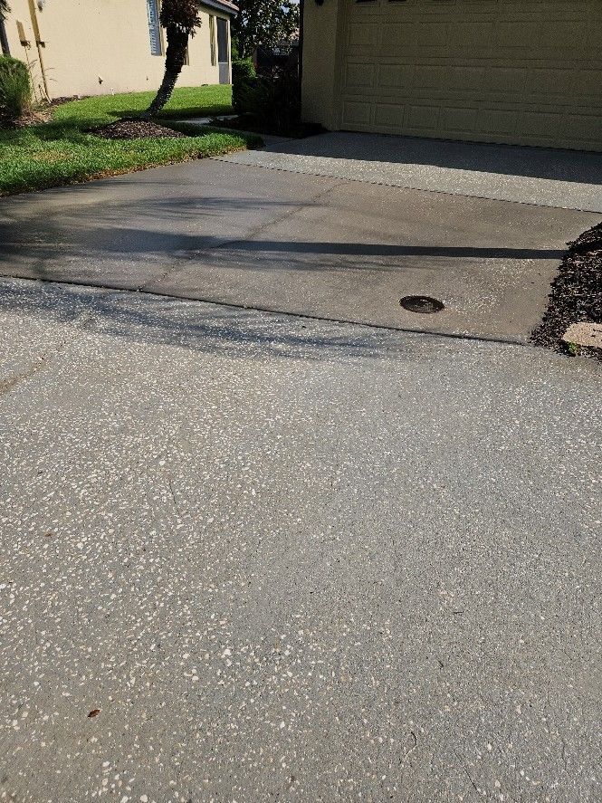 Cracked driveway leading to a garage, with a small drain cover near the center.