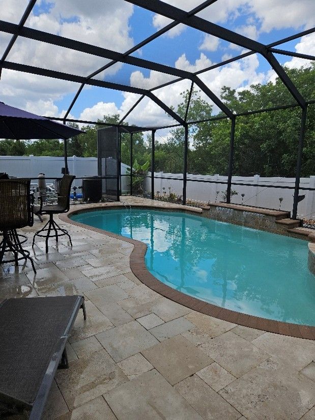 Screened-in backyard pool with stone deck and blue sky overhead