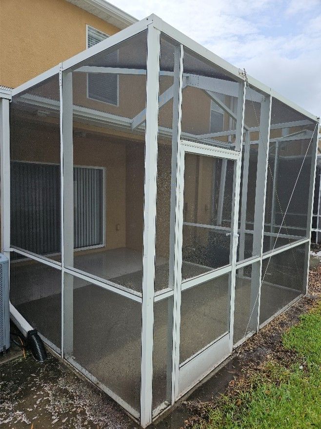 White screened patio enclosure attached to a house beside a grassy yard.