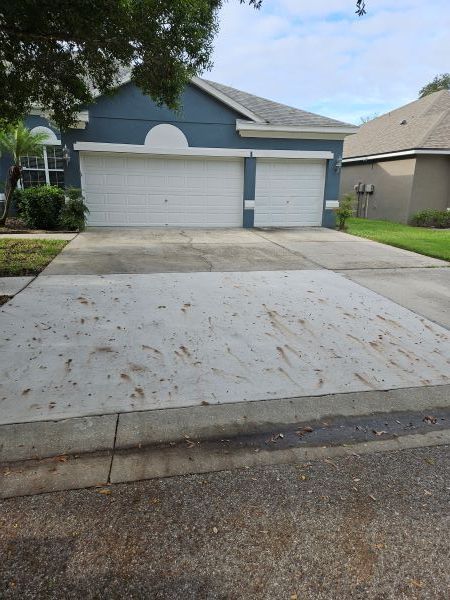 Suburban driveway and two-car garage with white doors and blue trim under a partly cloudy sky